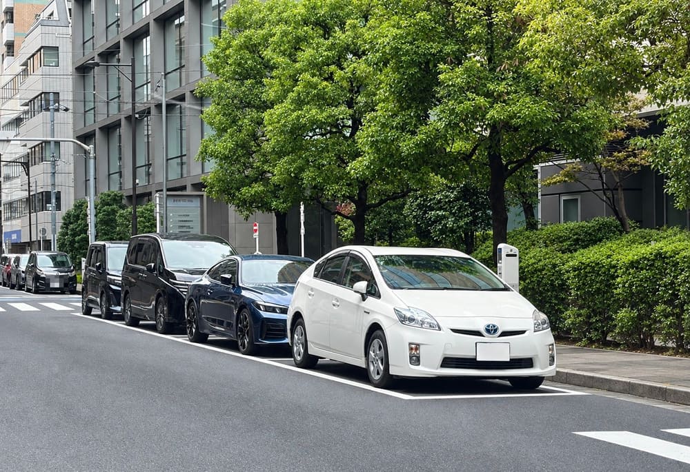 Cars parked in a row of white-lined parking spaces along the curb, with a parking meter on the sidewalk